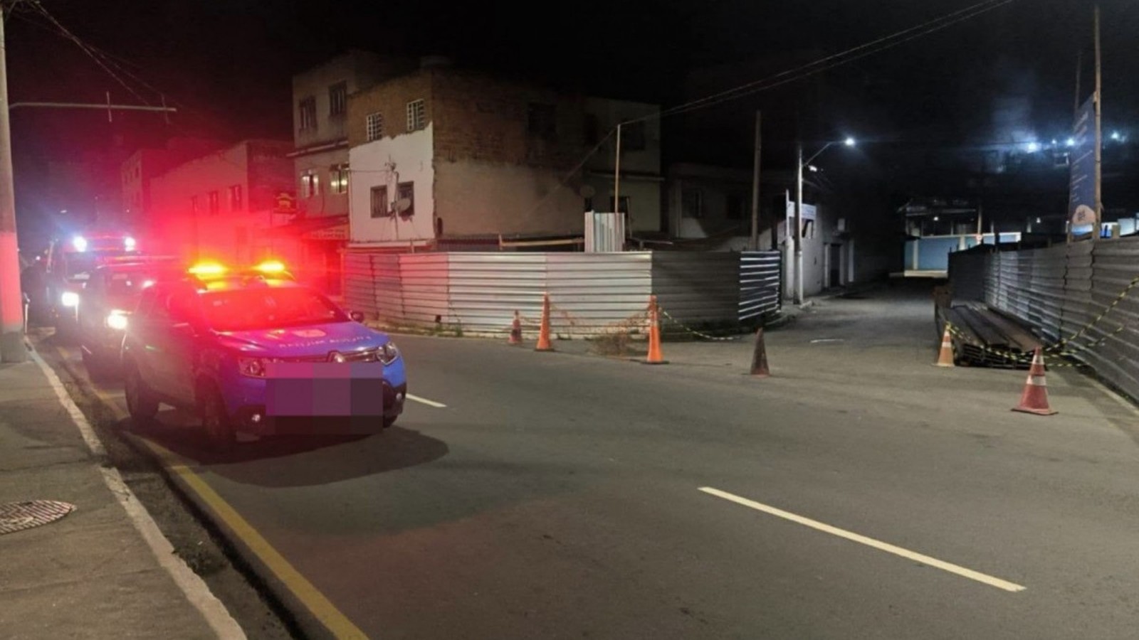 Duas viaturas policiais com luzes de emergência em rua escura com cones e cercas