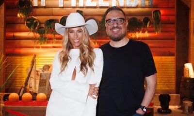 Rodrigo Carelli com óculos e mulher loira de chapéu de cowboy branco em cenário rústico