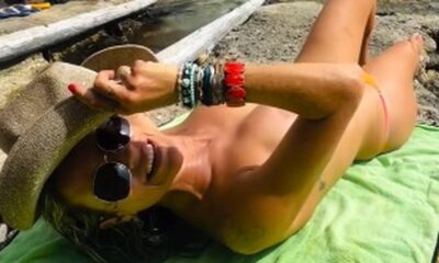 Mulher deitada de costas sem roupa em uma toalha verde, chapéu e óculos escuros