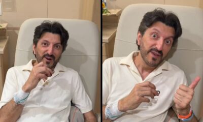 Homem branco de meia-idade, Lito Sousa, em cadeira médica, atadura no braço, fazendo 'joinha'