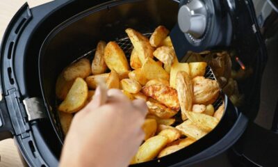 Mão de pessoa mexendo batatas rústicas douradas dentro do cesto de uma airfryer preta