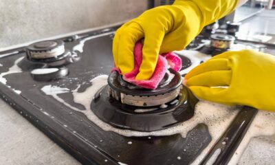 Mãos com luvas amarelas limpam queimador de fogão a gás com pano rosa e espuma