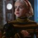 Sabrina Spellman segura um gato preto, usando blusa listrada e bandana vermelha, com olhar sério
