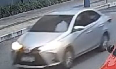 Carro sedan prateado com farol aceso em baixa qualidade de câmera de segurança