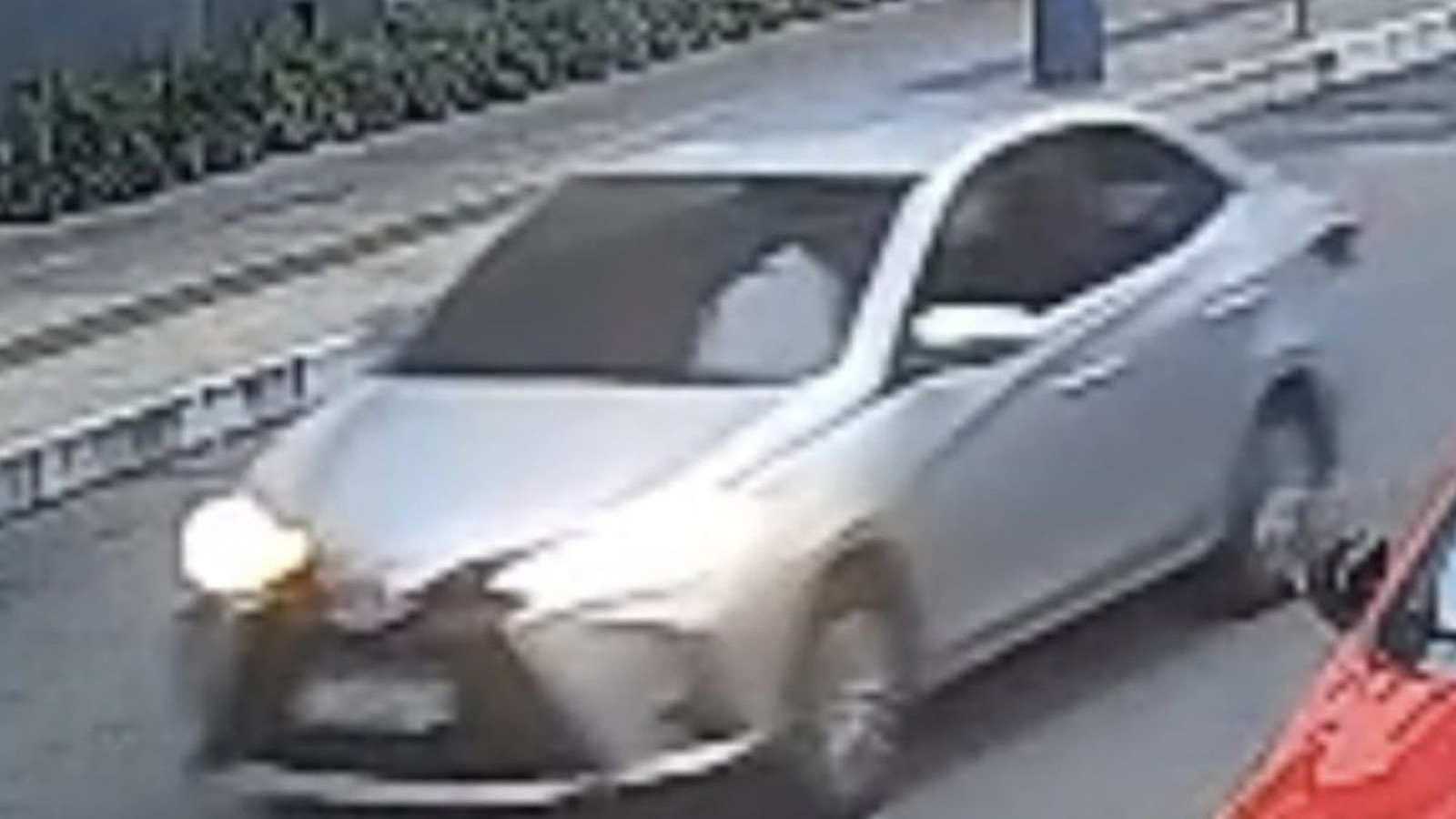 Carro sedan prateado com farol aceso em baixa qualidade de câmera de segurança