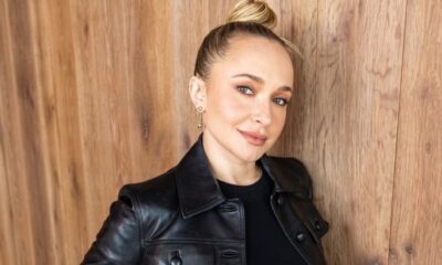 Hayden Panettiere, loira com coque, vestindo jaqueta de couro preta, sorrindo contra fundo de madeira