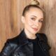 Hayden Panettiere, loira com coque, vestindo jaqueta de couro preta, sorrindo contra fundo de madeira