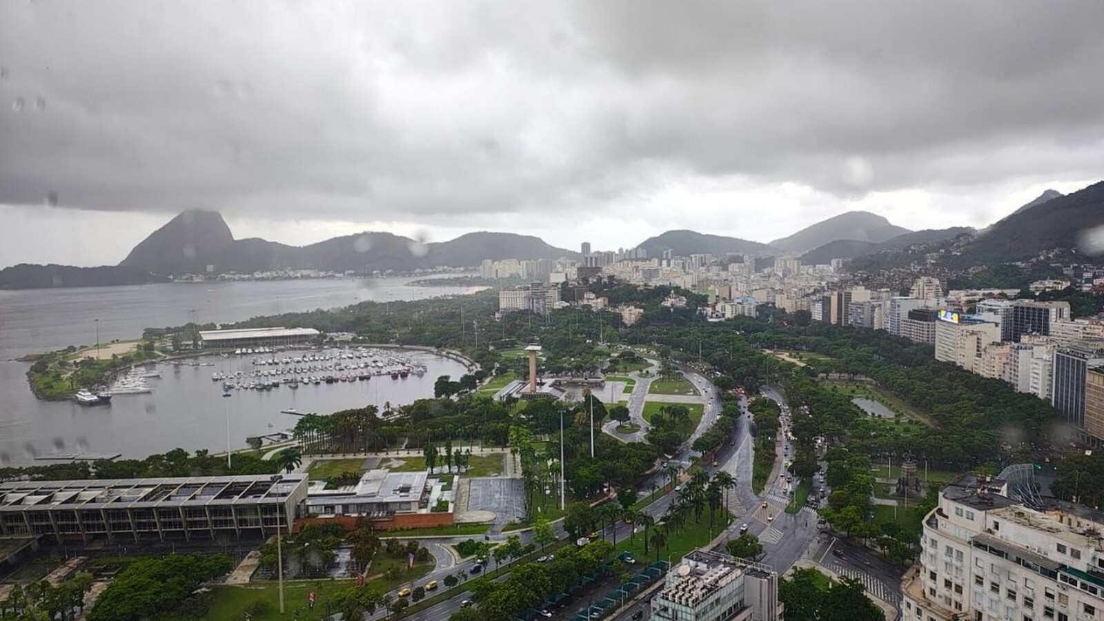 Vista aérea do Rio de Janeiro em dia nublado, com montanhas, marina e edifícios