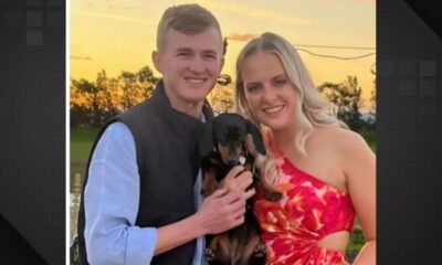 Casal sorrindo, homem e mulher, segurando um cachorro dachshund preto e marrom
