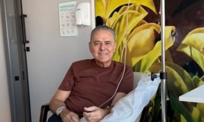 Homem sorrindo com soro intravenoso no braço, sentado em sala com placa de higiene das mãos