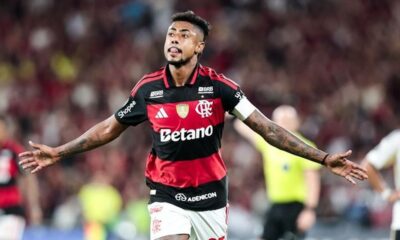 Jogador de futebol Bruno Henrique do Flamengo em camisa vermelha e preta, braços abertos, língua para fora