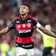 Jogador de futebol Bruno Henrique do Flamengo em camisa vermelha e preta, braços abertos, língua para fora