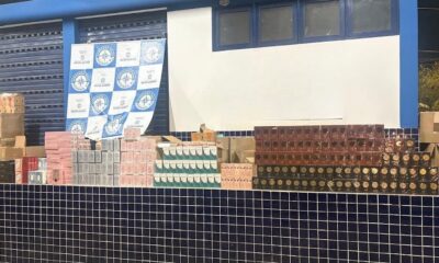 Pilhas de caixas de mercadorias irregulares, incluindo garrafas, diante de banner da Operação Foco