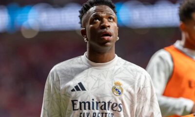 Close-up de Vinicius Júnior, pele escura, cabelo curto, olhando para cima, vestindo camisa branca do Real Madrid