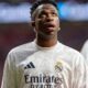 Close-up de Vinicius Júnior, pele escura, cabelo curto, olhando para cima, vestindo camisa branca do Real Madrid