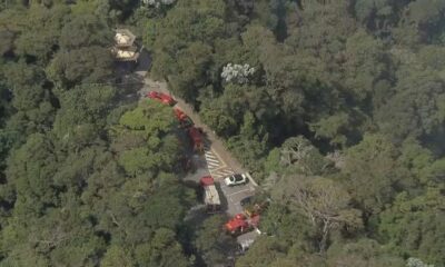 Vista aérea de estrada em floresta densa com viaturas de emergência e uma estrutura de pagode