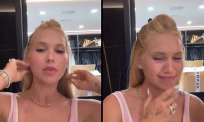 Mulher loira de blusa rosa e colar dourado em close, tocando cabelo e sorrindo em closet
