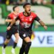 Jogador do Athletico-PR em camisa preta/vermelha (Umbro, Viva Sorte) celebra em campo verde
