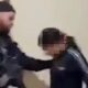 Dois policiais em uniforme escuro detêm uma mulher com o rosto borrado e capuz