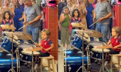 Menino de cabelos encaracolados toca bateria azul profissional em apresentação, público assiste