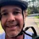 Close-up de homem sorrindo com capacete de bicicleta em trilha externa com árvores