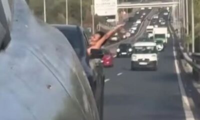 Mulher com blusa preta inclinada para fora da janela de carro em rodovia movimentada