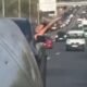 Mulher com blusa preta inclinada para fora da janela de carro em rodovia movimentada