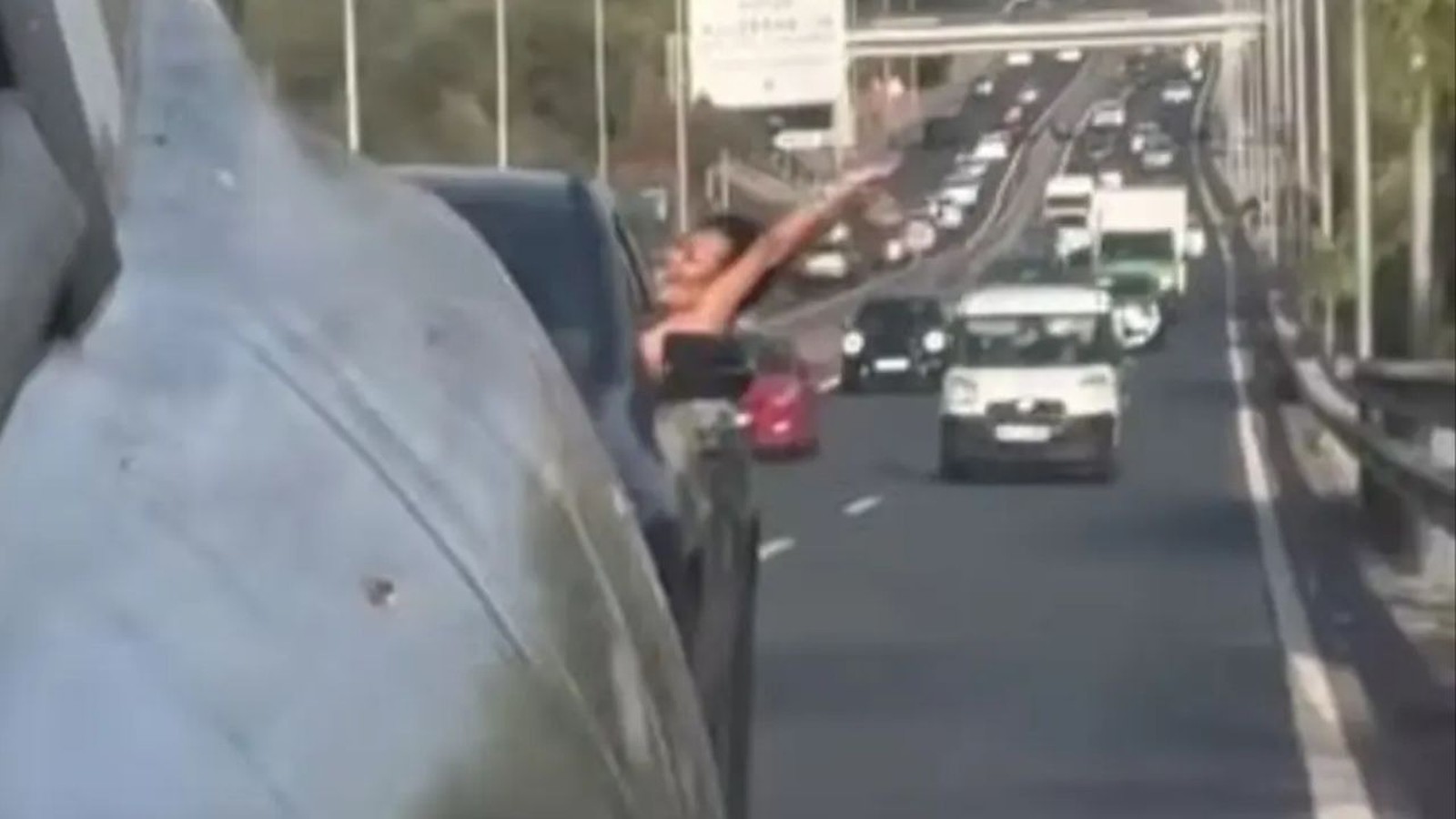 Mulher com blusa preta inclinada para fora da janela de carro em rodovia movimentada