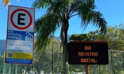 Placa de estacionamento Rio Rotativo Digital e painel luminoso em área verde com palmeira.