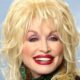 Dolly Parton sorrindo, cabelo loiro, batom vermelho, maquiagem roxa, brincos verdes