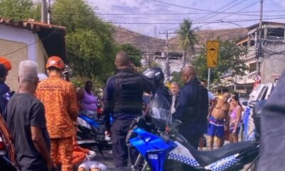 Homens da polícia e bombeiros em uma rua, com motocicletas e um corpo no chão