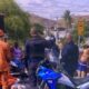 Homens da polícia e bombeiros em uma rua, com motocicletas e um corpo no chão