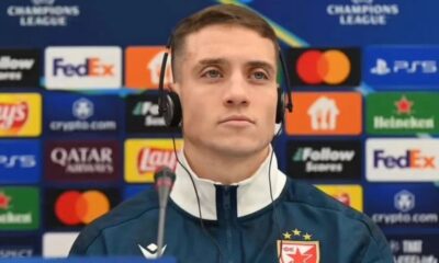 Futebolista com fones e microfone em coletiva da Champions League com logos de patrocinadores