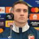 Futebolista com fones e microfone em coletiva da Champions League com logos de patrocinadores