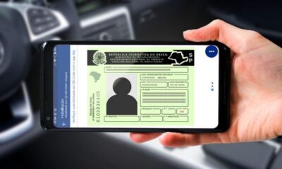 Mão segura celular exibindo CNH Digital brasileira com fundo de carro embaçado