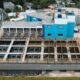 Vista aérea de estação de tratamento de água com tanques, edifícios azuis, e tanques circulares