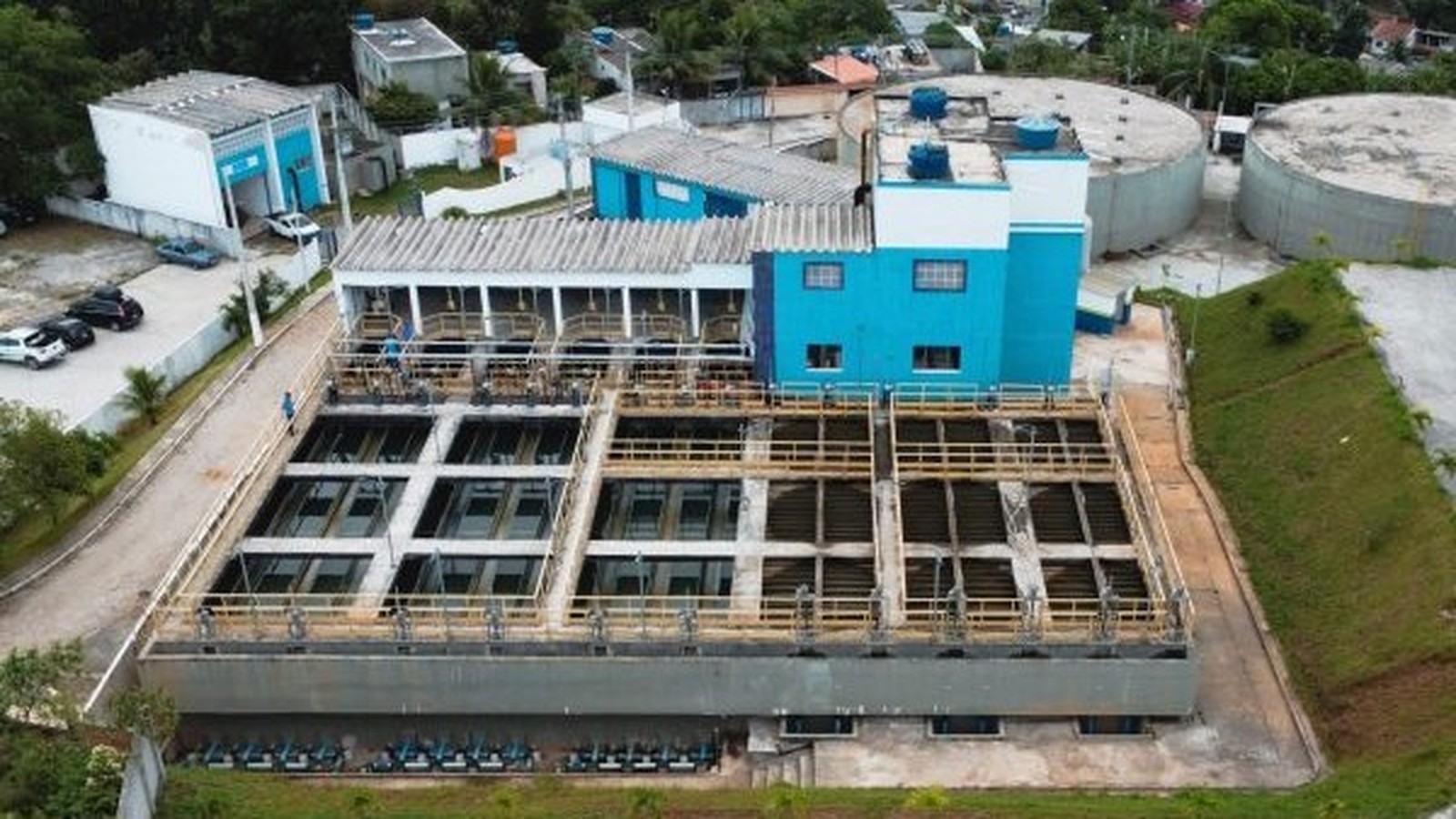 Vista aérea de estação de tratamento de água com tanques, edifícios azuis, e tanques circulares