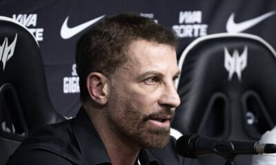 Homem barbudo de camisa preta fala ao microfone, fundo com logos Nike e Predator