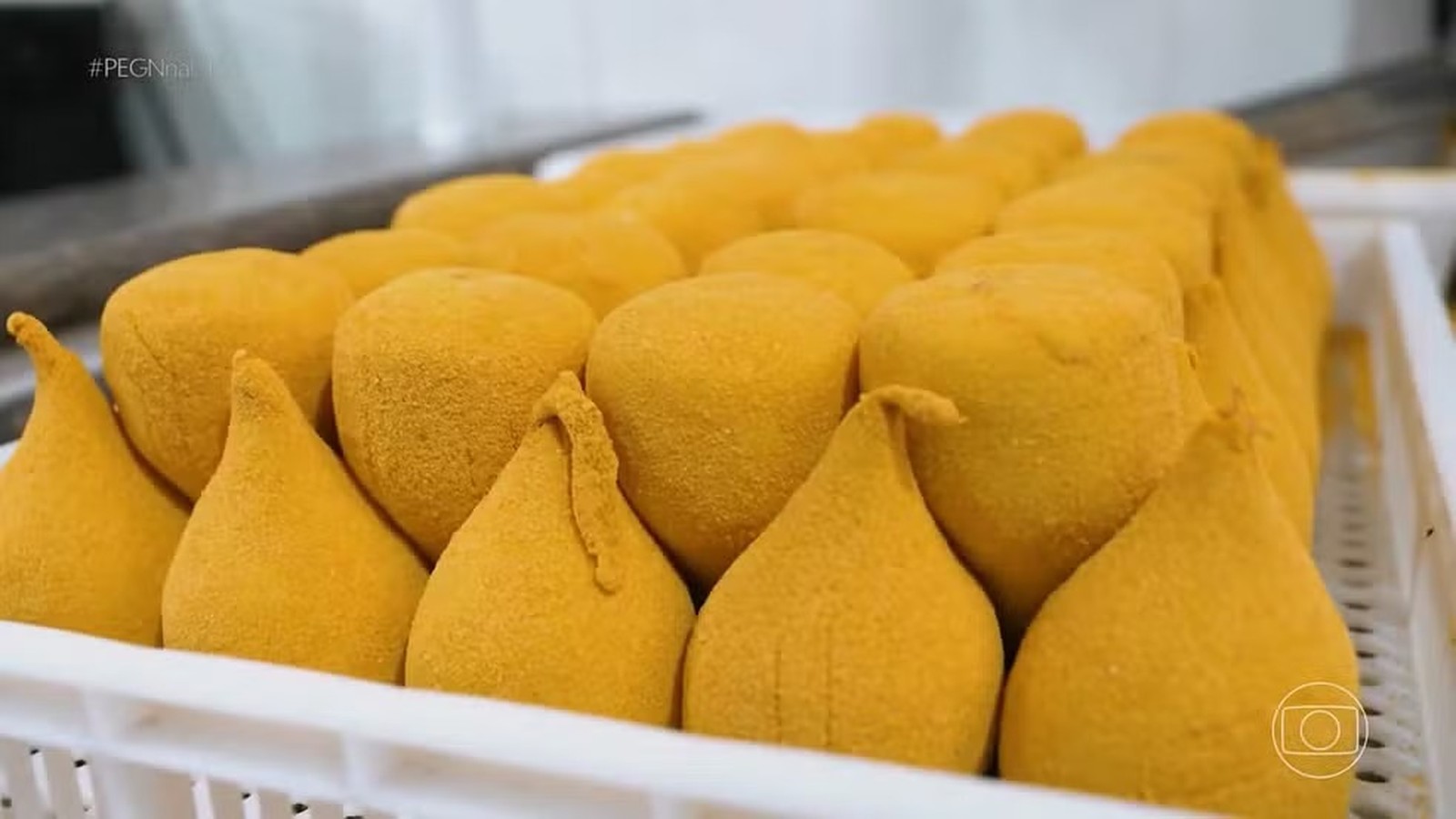 Dezenas de coxinhas e salgados empanados amarelos em bandejas brancas