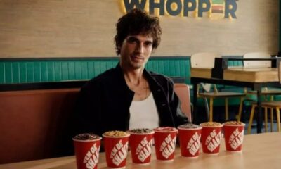 Fiuk sentado em restaurante Burger King, sorrindo para a câmera, com sete shakes em copos vermelhos