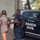 Policial escolta mulher ao lado de viatura preta da Polícia Civil com escudo e número "67-2754"