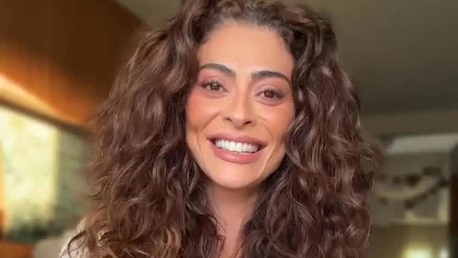 Rosto de Juliana Paes em close-up, sorrindo com cabelo cacheado castanho