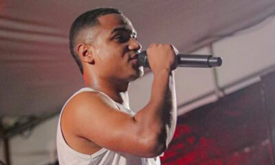 Jovem cantor suado segura microfone e canta em palco com iluminação vermelha
