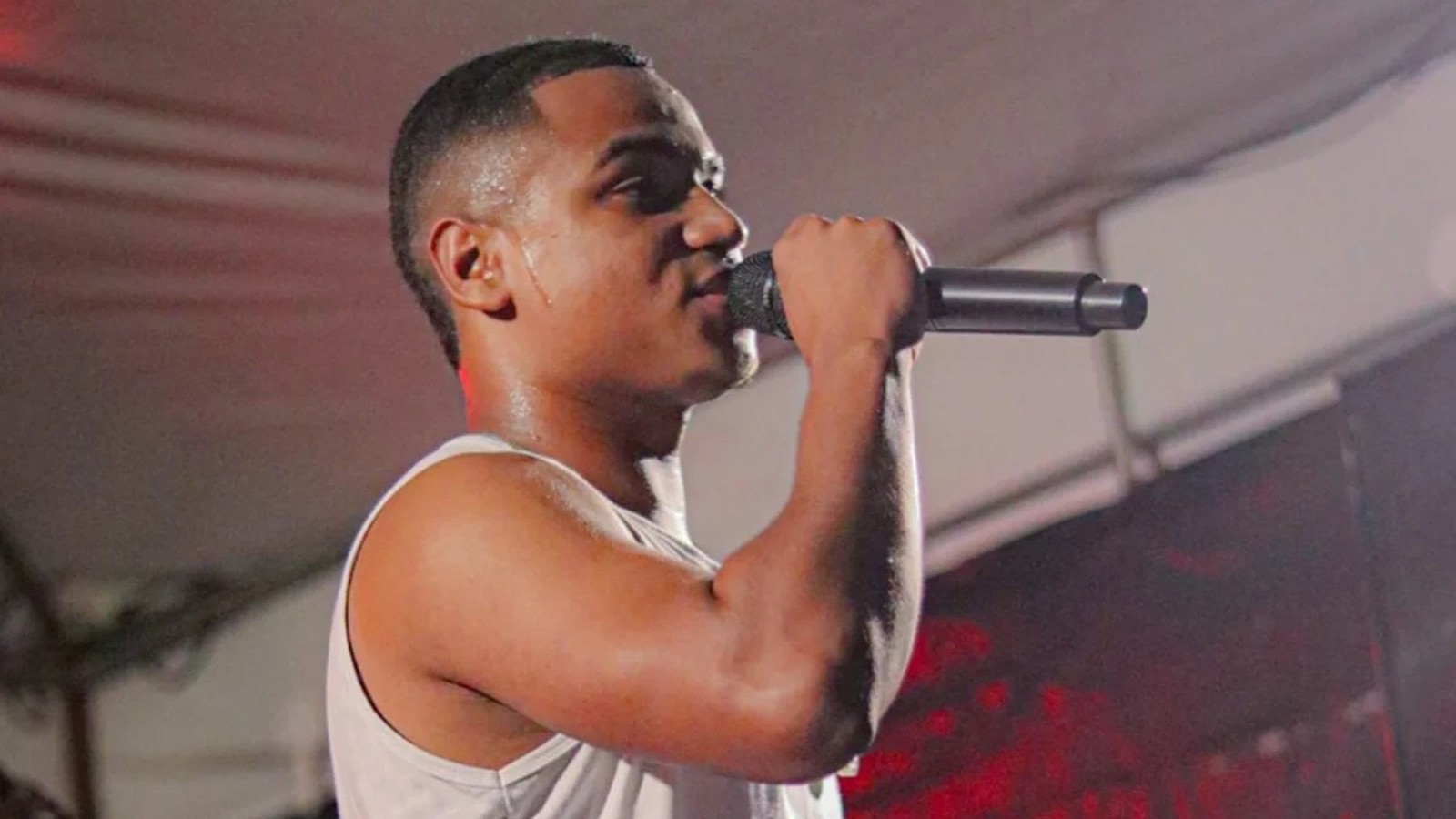 Jovem cantor suado segura microfone e canta em palco com iluminação vermelha