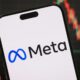 Smartphone com logotipo e nome Meta em tela, e gráfico financeiro desfocado ao fundo
