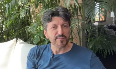 Homem de meia-idade com barba grisalha e camiseta azul em ambiente com plantas e janela