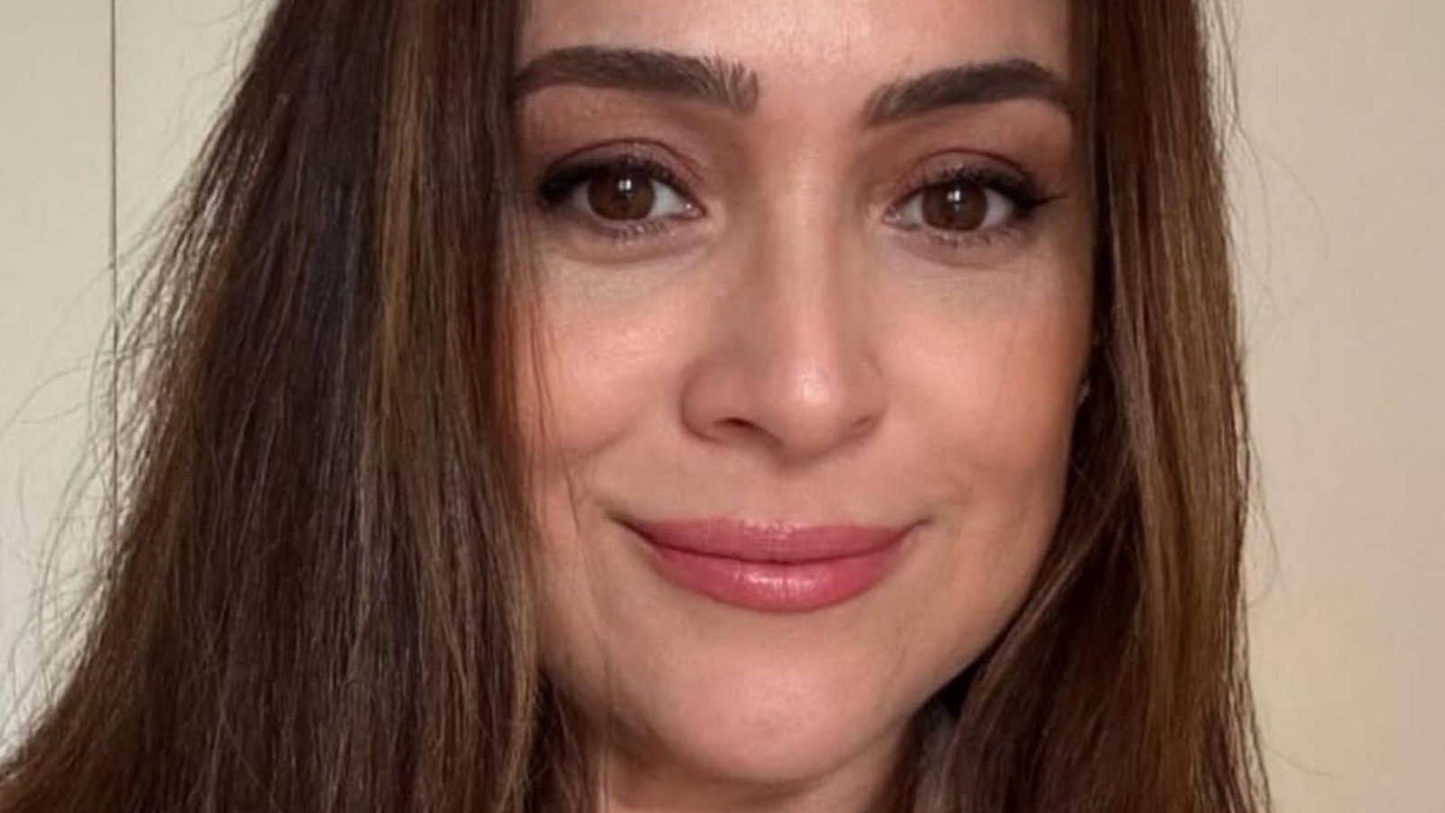 Mulher com cabelos e olhos castanhos, maquiagem leve, olhando para frente e sorrindo