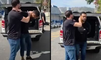 Homem detém outro homem ao lado de picape branca com porta-malas aberto na rua