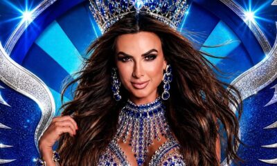 Nicole Bahls sorrindo, com coroa azul, joias exuberantes, em fundo carnavalesco azul e prata