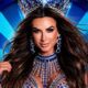 Nicole Bahls sorrindo, com coroa azul, joias exuberantes, em fundo carnavalesco azul e prata